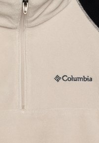 Beżowa polarowa bluza z zamkiem, z czarnym panelem na ramieniu. Posiada zamek z przodu oraz wyszywane logo Columbia w ciemnoniebieskim kolorze. Miękka tekstura.