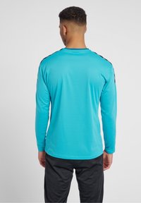 Langärmliges Shirt aus leuchtend türkisfarbenem Polyester mit schwarzen Akzenten an den Schultern, mit einem runden Ausschnitt und taillierter Passform.