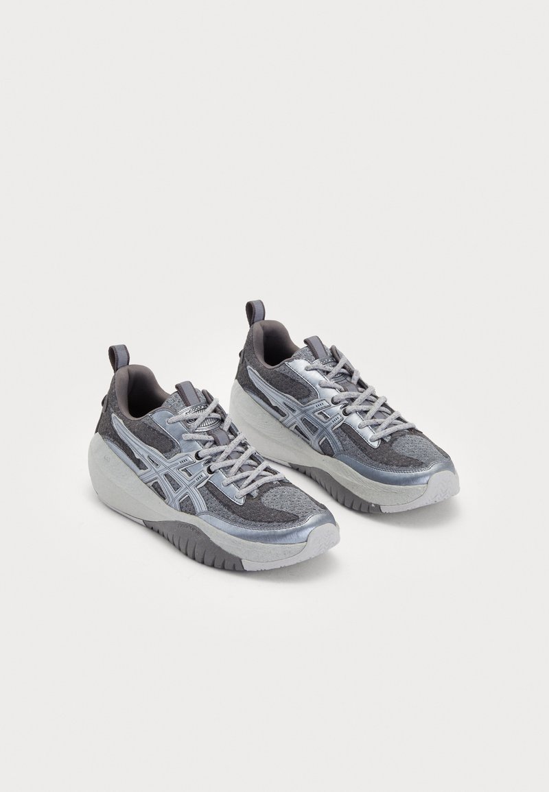 Sportos sportcipők szürke, textúrázott felsőrésszel, ezüst kiegészítőkkel és masszív talppal. Fűzős kialakítás és húzófülek a könnyű felhúzáshoz.