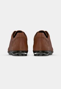 Paire de chaussures en cuir marron avec semelles noires vues de dos sur un fond clair uni.