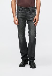 Jeans de mezclilla gris con un corte recto, lavado desvanecido, bolsillos frontales y sutiles detalles de costura, combinados con zapatos negros.