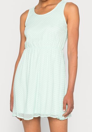 Robe sans manches vert menthe clair avec une taille froncée et un motif à pois. Tissu fluide avec une finition légèrement translucide et un col arrondi.