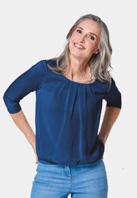 Marineblaue Bluse mit Dreiviertelärmeln, gepeitschter Vorderteil-Detail und rundem Ausschnitt. Glatter Stoff, lockere Passform, getragen mit heller Denim.