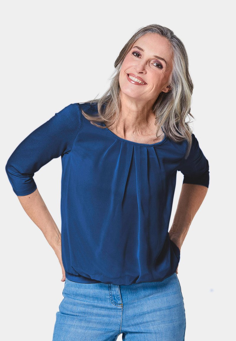Marineblaue Bluse mit Dreiviertelärmeln, gepeitschter Vorderteil-Detail und rundem Ausschnitt. Glatter Stoff, lockere Passform, getragen mit heller Denim.