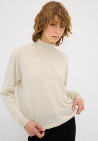 Crème turtleneck sweater met verhoogde parelaccenten, gestructureerd oppervlak, lange mouwen en een relaxte pasvorm. Subtiele glans.