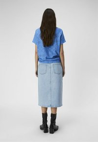 Das blaue Oberteil mit Stickereien hat kurze Ärmel und einen lockeren Schnitt und wird mit einem leichten Denim-Midirock und schwarzen Stiefeln mit Absatz kombiniert.