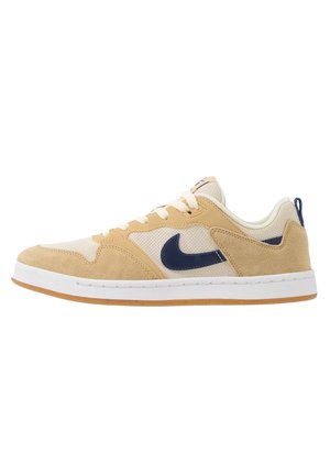 Zapatilla baja con paneles de ante beige y malla, logo Nike en azul marino, cordones blancos y suela de goma natural.
