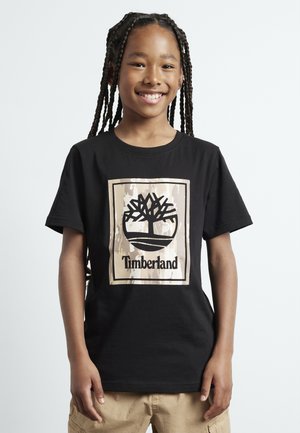 T-shirt en coton noir avec un logo d'arbre en noir et beige, portant le mot "Timberland" en dessous, manches courtes et col rond.