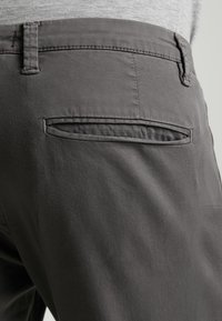 Grå byxor med en slät tygkvalitet, slim fit, och en enda bakficka med horisontell öppning. Rena sömmar synliga.