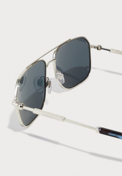 Metal aviator sunglasses with dark lenses, featuring a silver frame, adjustable nose pads, and elongated silver arms with textured accents.