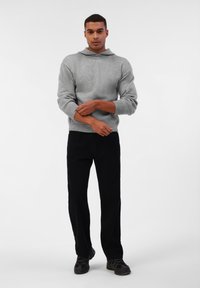 Grijze gebreide hoodie met een relaxte pasvorm, geribbelde manchetten en een kangoeroezak, gecombineerd met zwarte rechte broek en donkere schoenen.