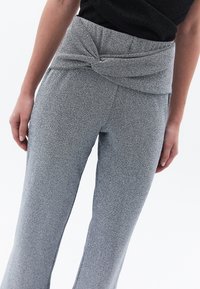 Rekkende grijze gebreide broek met een gestructureerde afwerking, voorzien van een knoopdetail in de taille en flared pijpen voor een comfortabele pasvorm.