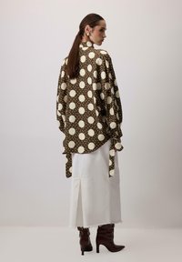 Camicia marrone a pois con colletto alto e maniche larghe, abbinata a una gonna di jeans bianca e stivali alti marroni.