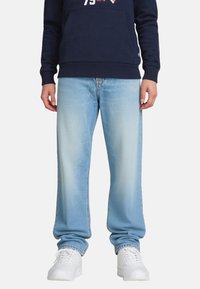 Jeans in denim azzurro chiaro con un taglio rilassato, caratterizzati da una finitura sbiadita e da leggeri segni di usura. Combinati con sneakers bianche da atletica.