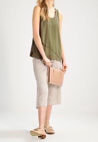 Olivgrön ärmlös topp med asymmetrisk nederdel, kombinerad med ljusbeiga cropped byxor och en liten rosa väska. Ljusfärgade skor med accenter.