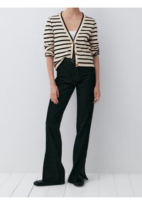 Sweter w paski w kolorze kremowym i czarnym, z trzema guzikami, zestawiony z ciemnoniebieskimi spodniami dzwonami o wysokim stanie i czarnymi balerinami.