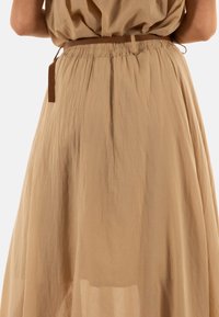 Larga y fluida falda beige hecha de una tela ligera, con una cintura elástica y un detalle de lazo marrón para un ajuste ajustable.