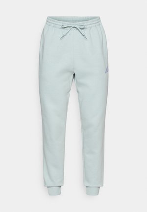 Jasnoniebieskie spodnie dresowe z elastycznym pasem i sznurkiem do regulacji. Mają zwężane nogawki z prążkowymi ściągaczami oraz małe fioletowe logo po bokach.