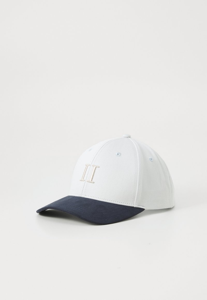 White baseball cap with a navy blue visor, featuring a beige "II" embroidered on the front. Made of textured fabric.