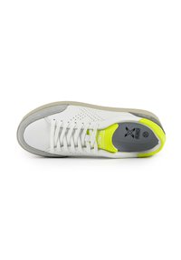 Sneakers bianchi con tomaia in pelle liscia, dettagli grigi, design perforato e un tacco posteriore giallo brillante. Lacci piatti e suola ammortizzata.