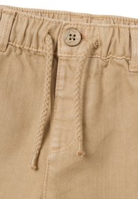 Bermudas de algodón beige con una cinturilla elástica, cordón trenzado y un detalle de botón de madera en la parte delantera. Presenta costuras cosidas.