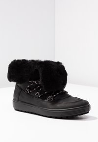 Bottes de neige noires avec un revers en fausse fourrure, tige en cuir texturé, lacets contrastants et une semelle en caoutchouc robuste pour une bonne traction.