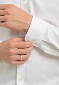 Vit skjorta med knappmanchett. Anmärkningsvärda egenskaper inkluderar en slät textur, pärlliknande knapp och skräddarsydd passform. Händer som justerar manchetten.