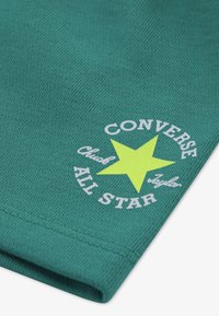 Πράσινο υφαντό ύφασμα με ένα μεγάλο κίτρινο αστέρι και λευκό κείμενο «CONVERSE» με τη φράση «Chuck Taylor All Star» από κάτω, στο κέντρο του σχεδίου.