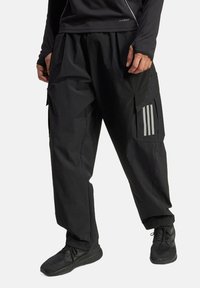 Black cargo pants with a loose fit, featuring side pockets, a textured fabric, and three vertical stripes on the left leg. Pairing with black shoes.