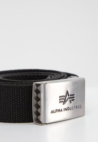 Cinturón tejido negro con un clasp de metal. El clasp presenta un logotipo y un borde serrado para un mejor agarre. El material es resistente y texturizado.