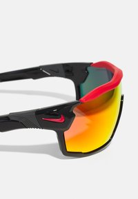 Schwarze Sportsonnenbrille mit einem umschließenden Design, ausgestattet mit einem roten Gummielement oben und getönten Gläsern, die von grün nach orange übergehen.