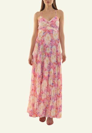 Frau trägt ein ärmelloses, plissiertes, bodenlanges Kleid mit einem floralen Muster in Pink, Lila und Weiß sowie dünnen Schulterträgern.