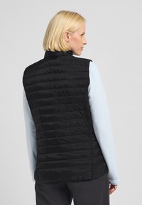 Gilet nero imbottito con cuciture orizzontali trapuntate, colletto alto e materiale leggero. Indossato sopra una maglietta a maniche lunghe azzurro chiaro.