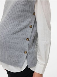 Šoninis vaizdas, kuriame matyti raštuotas pilkas megztinis su keturiais rudi mygtukais, dėvimas virš baltos ilgos rankovės marškinių ir juodų kelnių.