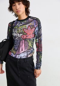 Langermet, flerfarget Adidas-genser med grafisk trykk og svarte treskipsdetaljer, paret med høy midje svarte bukser.