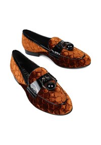 Para brązowych welurowych mokasynów z tłoczonym okrągłym wzorem, czarnym lakierowanym paskiem i dekoracyjnym czarnym koralikowym detalem na białym tle.