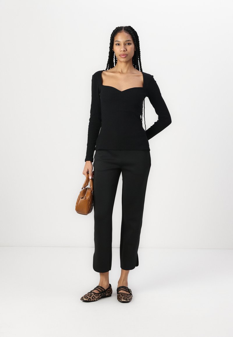 Czarna, prążkowana, długi rękaw bluzka z dekoltem w kształcie serca, w zestawieniu z czarnymi, dopasowanymi spodniami oraz płaskimi butami w panterkę. Trzyma brązową torebkę.