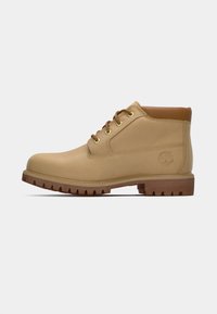 Beige lær ankle boots med en glat overflade, brune accenter, gyldne øjer og en tekstureret gummisål med et lugmønster.