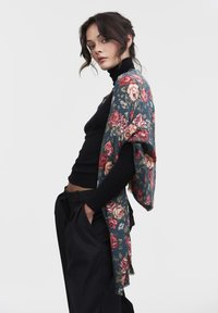 Bloemen sjaal in donkerblauw met rozenpatronen; zachte stof, franjes aan de randen, gedragen over een zwarte coltrui, gecombineerd met zwarte broek.