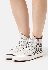 Höga sneakers i kanvas i krämfärgad med svart rutmönster, vita snören, gummisålar och varumärkeslogotyp på tungan.