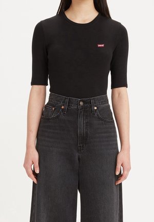 Czarny krótki top z okrągłym dekoltem i czerwoną naszywką z logo Levi's; w połączeniu z wysokim stanem ciemnoszarych dżinsów z guzikowym zapięciem.