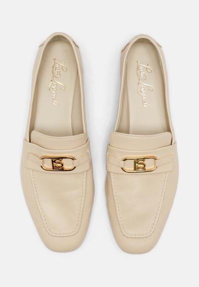 Mocassins en cuir beige avec un bout arrondi, une semelle plate et un fermoir accentué en or à l'avant. Texture lisse, design minimaliste.