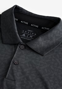 Schwarzes gemustertes Poloshirt mit umgeschlagenem Kragen und zwei Knöpfen, Größe Medium, Marke "NEXT ACTIVE", hergestellt in Kambodscha.