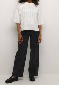 Pull en tricot blanc avec un motif de feuilles texturé, associé à un jean en denim noir ample et des chaussures noires brillantes.