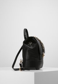 Czarny skórzany plecak o fakturowanej powierzchni, zaokrąglonym kształcie, złotych akcentach metalowych, bocznej rączce i regulowanym pasku do uniwersalnego noszenia.