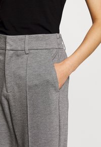 Pantaloni grigi su misura con una texture liscia, dotati di tasche laterali e un design frontale piatto. La vita è leggermente elastica per un maggiore comfort.