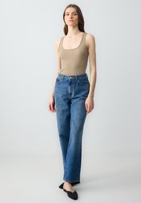 Beige geribbelde bodysuit, high-waisted blauwe denim jeans met rechte pijpen en lichte slijtage, gecombineerd met zwarte instap schoenen.