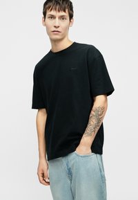 Μαύρο βαμβακερό T-shirt με στρογγυλή λαιμόκοψη και κοντά μανίκια. Διαθέτει ένα μικρό, τονικό λογότυπο στο στήθος και έχει χαλαρή εφαρμογή.