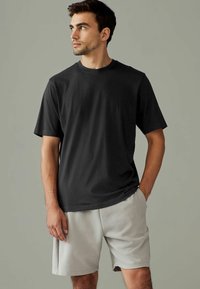 Camiseta negra de manga corta hecha de algodón, con un clásico cuello redondo. Combinada con pantalones cortos deportivos grises claros, ambos tienen una textura suave.