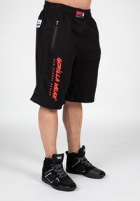 Black shorts featuring a textured fabric, a zippered pocket, and bold red "GORILLA WEAR" branding on the left side. Black athletic shoes.